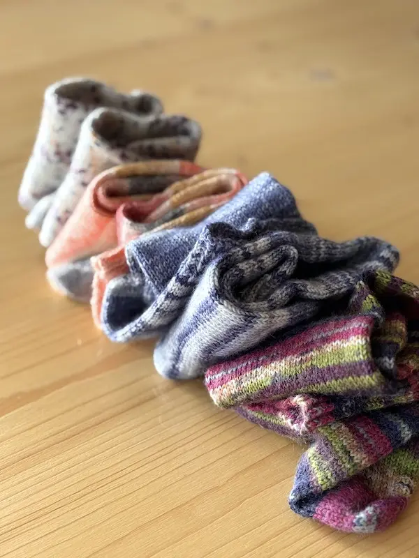 Pile de chaussettes tricotées main en laine fingering colorée, illustrant la diversité des fils et motifs du tricot de chaussettes.