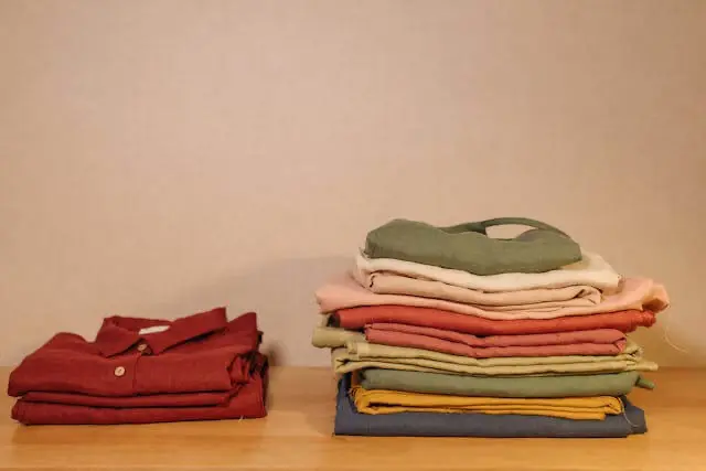 Piles de vêtements en lin et coton dans des tons naturels – beige, rose poudré, vert sauge et ocre – illustrant l’harmonie des couleurs et des matières.