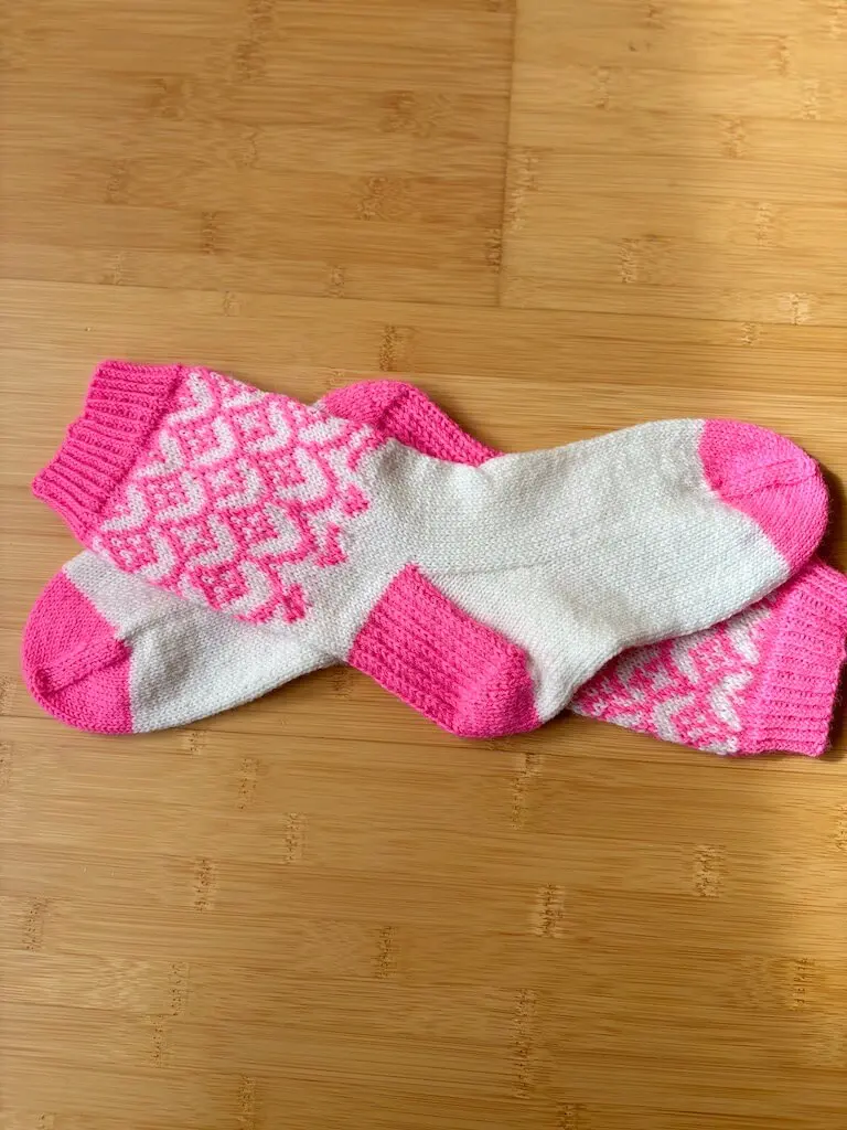 Paire de chaussettes jacquard rose et blanc Début tendre terminée, posée à plat sur une surface en bois