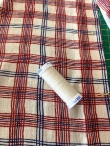 Bobine de fil écru fournie dans la box couture Gariguette, posée sur la viscose à carreaux
