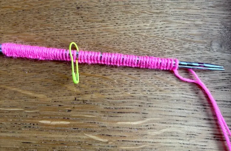 Montage long tail cast on en laine rose réalisé sur deux aiguilles tenues ensemble pour garder un bord souple